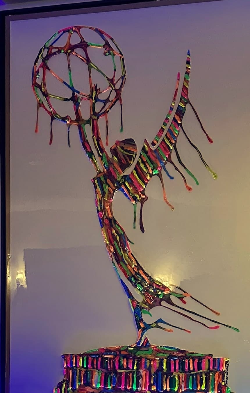 A winged statuette figure rendered in dripping bands of rainbow colour on a white ground.