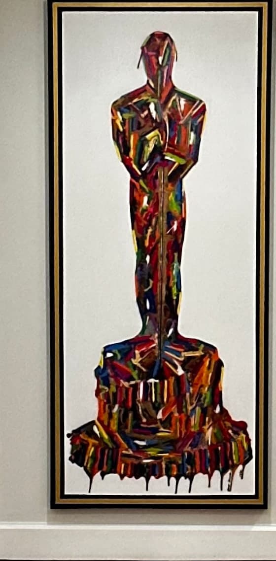 A standing human figure built from interlocking strokes of vivid colour, the paint dripping at the base, in a black and gold frame.