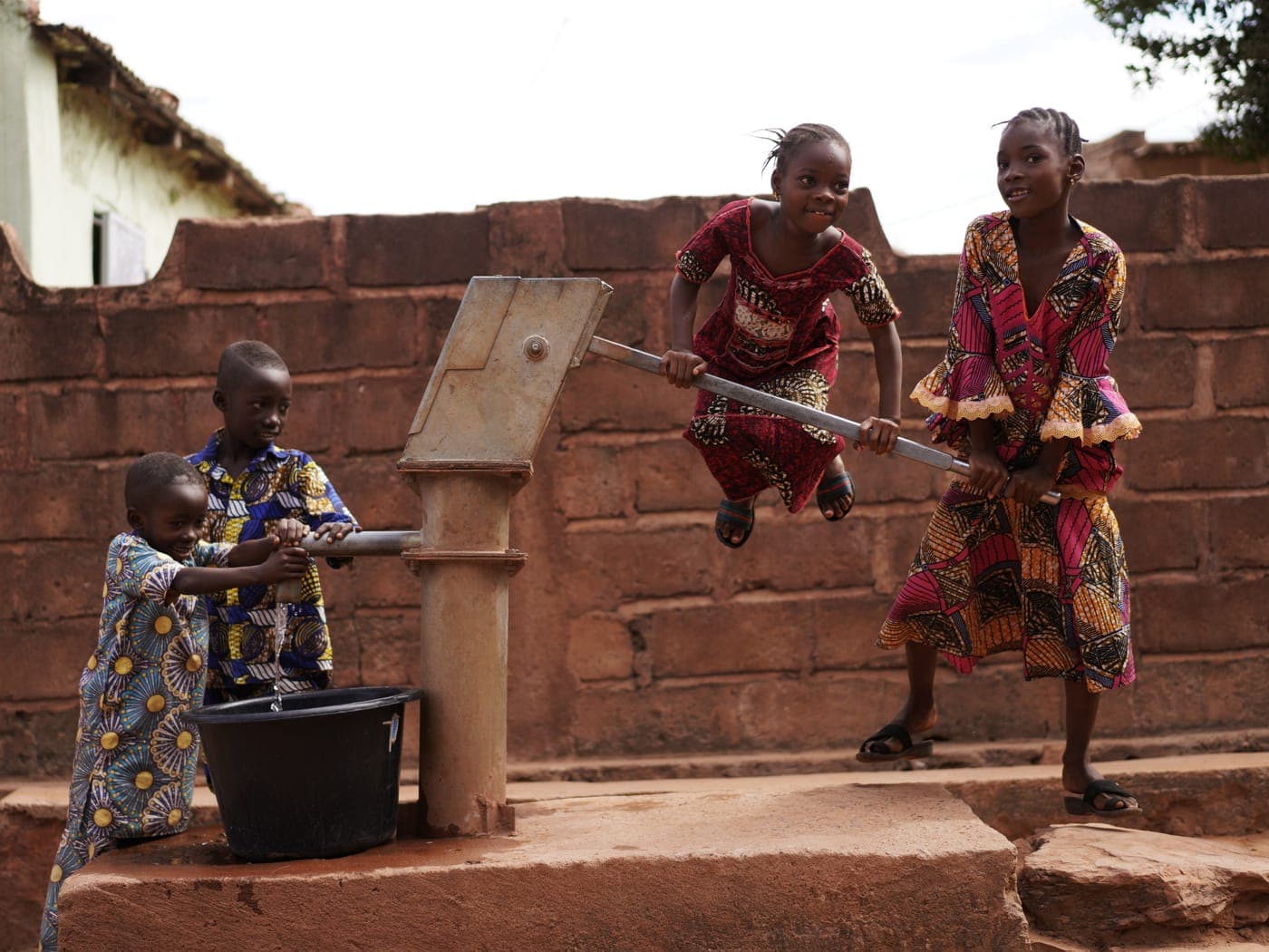 A hand pump at a village water point with a maintained concrete apron.
